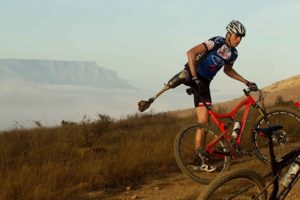Reuben Van Niekerk dismounts his bicycle to help fellow amputee and team-mate Dane Wilson with a technical problem during the prologue of the 2013 Absa Cape Epic Mountain Bike stage race on March 17, 2013. Photo: Greg Beadle / Cape Epic / SPORTZPICS