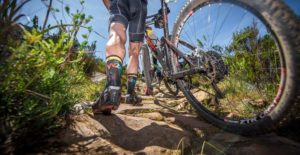 A rider jumps off the saddle to push his bike up a rocky section of the Wines2Whales Ride route.